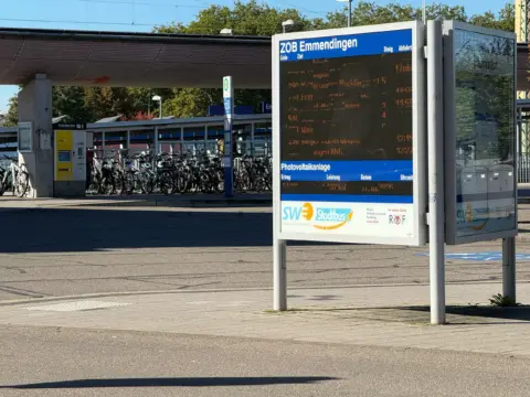 Bus station in Emmendingen with a tall digital timetable/display and a bicycle rack nearby under a shelter.