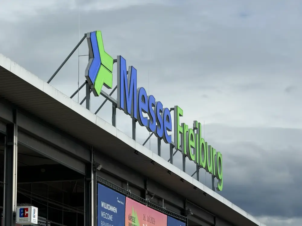 Close-up of blue and green 'Messe' sign on a modern convention center under a cloudy sky.